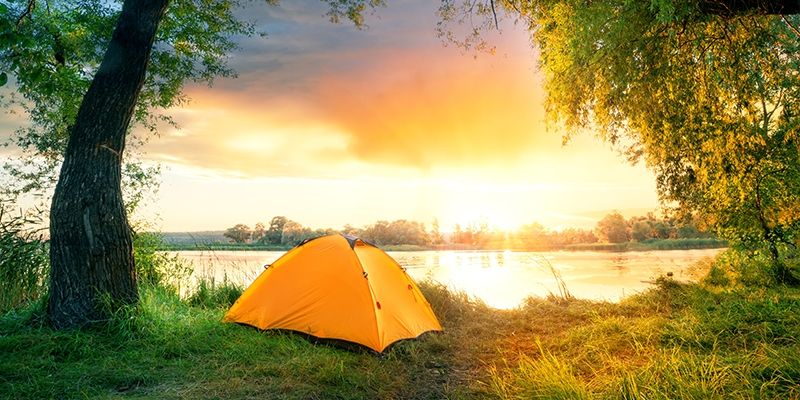 Ein Zelt steht während des Sonnenuntergangs am See.