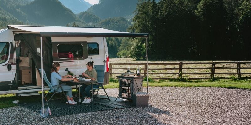 Zwei Freunde genießen die Zeit vor dem möbilierten Campervan. 