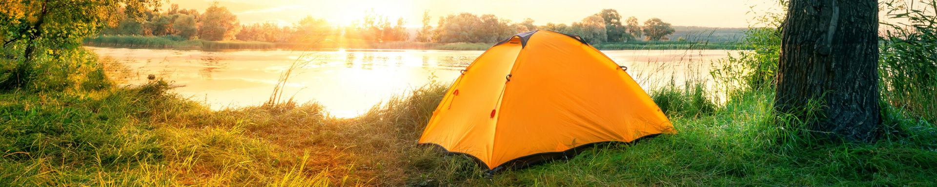 Ein Zelt steht während des Sonnenuntergangs am See.